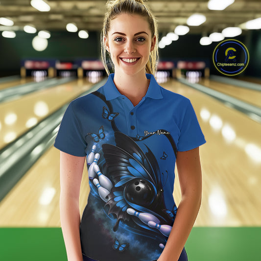 Female model at a bowling lane wearing a blue and black bowling polo shirt with butterfly artwork, a bowling ball, and pin graphics.