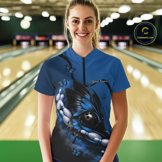 Female model shown from the front in a bowling venue wearing a blue and black quarter-zip shirt with butterfly and bowling-themed graphics.