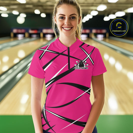Front view of a female bowler wearing a pink, black, and white bowling quarter zip shirt in a bowling alley