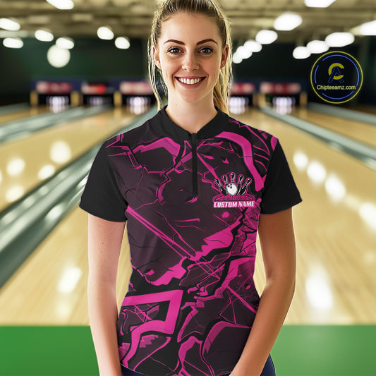 Female model wearing a black and pink quarter-zip in a bowling center with angular geometric artwork and cracked design elements.