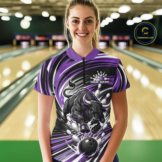 A woman stands in a bowling alley wearing a short-sleeve quarter zip bowling jersey with a purple, black, and white bull graphic and the text 'YOUR NAME'.