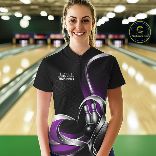 Female model at a bowling lane wearing a black and purple quarter zip shirt, showcasing a honeycomb pattern with a heart framing a bowling ball and pins.