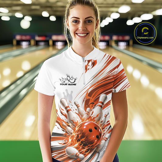 A woman wearing a white short-sleeve bowling-themed shirt with a dynamic orange and white bowling ball graphic, standing in a bowling alley. The shirt features a white base with orange and white abstract streaks and a large bowling ball and pins design on the front.