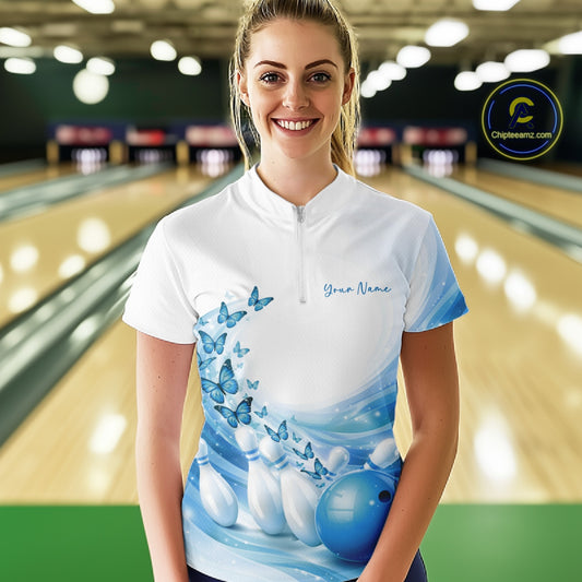 Front view of a female model in a white and blue bowling quarter zip with butterfly accents and bowling graphics inside a bowling alley.