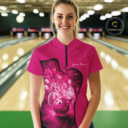 Female model in a pink bowling quarter zip featuring butterfly graphics and bowling artwork, front view inside a bowling alley