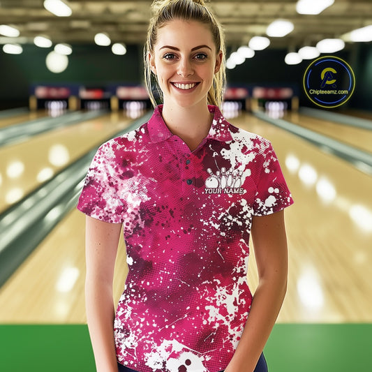 Woman wearing a pink and white patterned bowling shirt with a logo and text in a bowling alley.