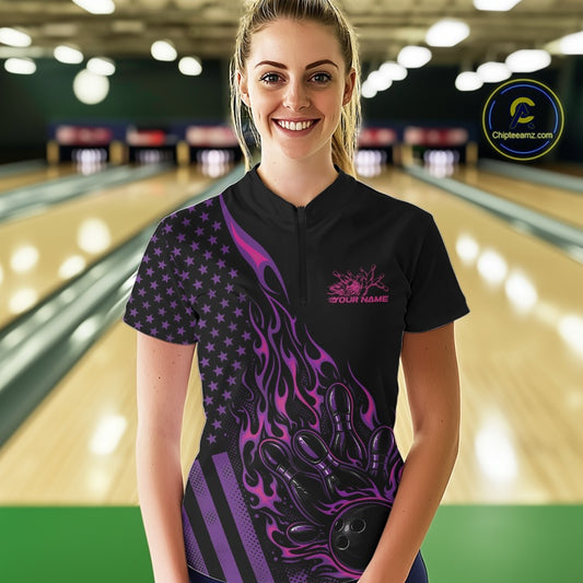 Female model at a bowling lane wearing a black bowling quarter-zip shirt with pink and purple flame bowling strike artwork and American flag accents.