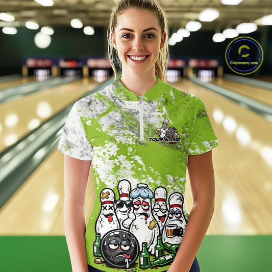 Front view of a female model in a bowling lane wearing a white quarter-zip shirt featuring green and white grunge splatter design with cartoon bowling pins and beer bottle scene.