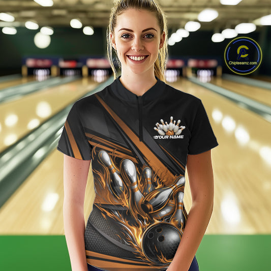 Female model in a bowling lane wearing a black quarter-zip shirt, gold flame bowling ball hitting pins with abstract sporty stripe design.