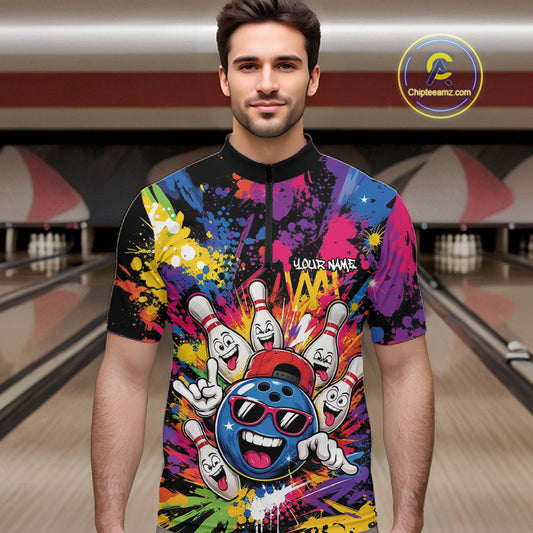 A man wearing a short-sleeve black quarter-zip bowling-themed shirt with a colorful paint splatter theme, cartoon bowling ball and pins graphic, standing in front of a bowling alley background.