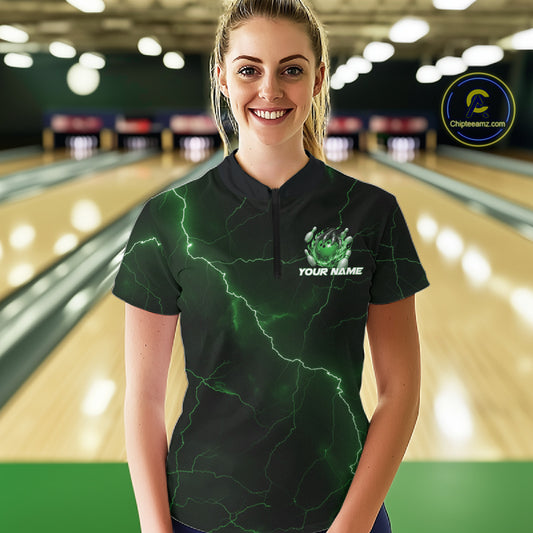 Female model wearing a black and green quarter-zip with dragon claw bowling artwork in a bowling lane.
