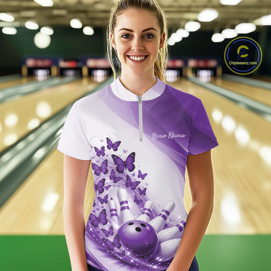 Female model wearing a white and purple bowling quarter zip with butterfly graphics and bowling artwork, front view at the bowling lane