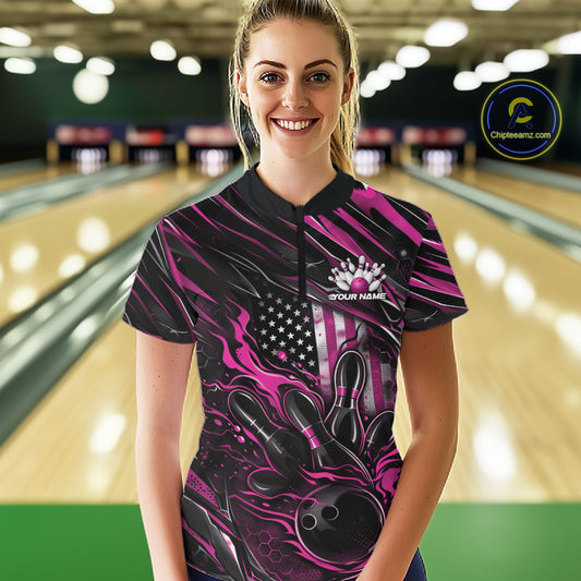 Female model in a bowling lane wearing black and pink quarter zip shirt, front view showcasing patriotic flames bowling ball hitting pins with energetic styling