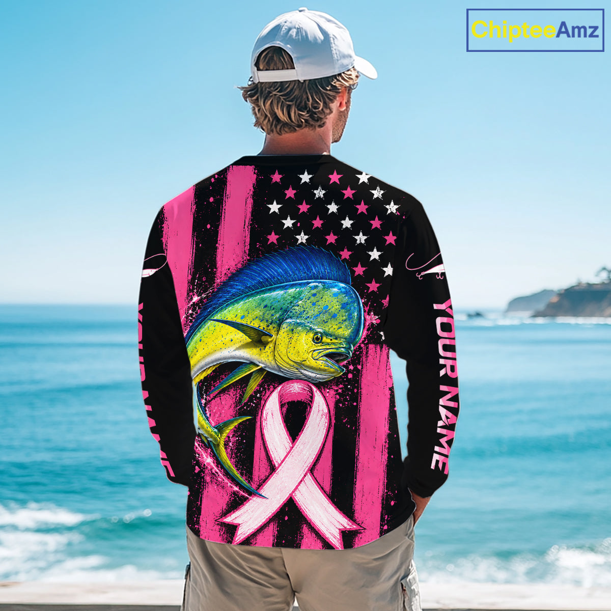A man viewed from behind wearing a long-sleeve black and pink graphic shirt with a large mahi mahi, pink ribbon, stars, and vertical 'YOUR NAME' text, standing by the ocean. The shirt has 'ChipteeAmz' branding in the top right corner.