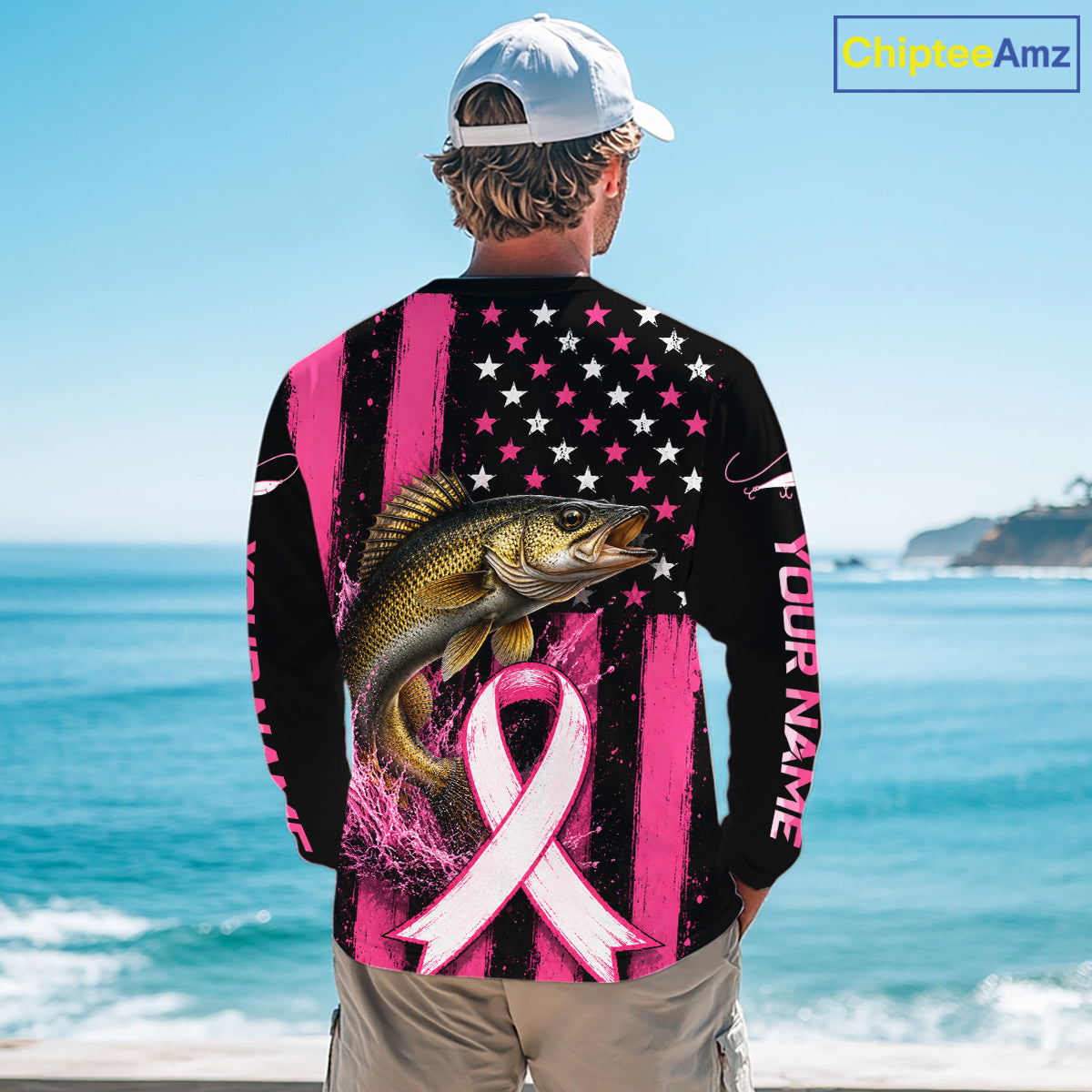 A man viewed from behind wearing a long-sleeve graphic shirt with a pink and black American flag design, a large bass fish, and a pink awareness ribbon on the back. The shirt also has 'YOUR NAME' printed on the sleeve.