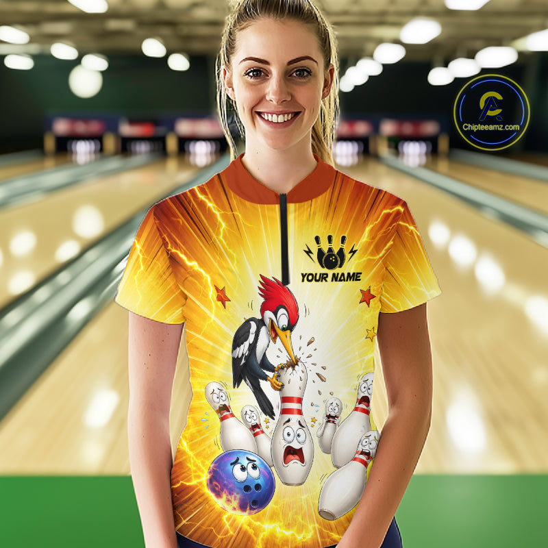 Person wearing a yellow bowling shirt with a cartoon design in a bowling alley.