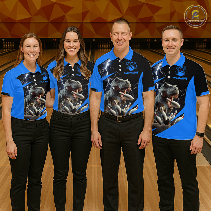 Four people standing in a bowling alley wearing matching custom-designed polo shirts with a blue and black color scheme, featuring a graphic of a roaring dinosaur and lightning, paired with black pants.