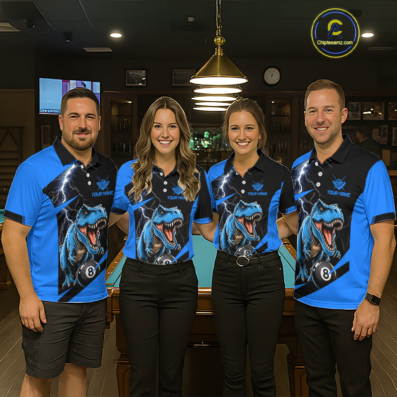 Four people standing together in a dimly lit indoor venue, each wearing matching blue and black polo shirts with a large blue dinosaur graphic and the text 'YOUR NAME' 