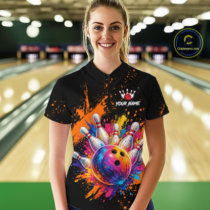 A woman wearing a black bowling-themed polo shirt with a colorful bowling ball and pins graphic, standing in a bowling alley. The shirt features a white crown logo, the text 'YOUR NAME', and a colorful paint-splatter design.
