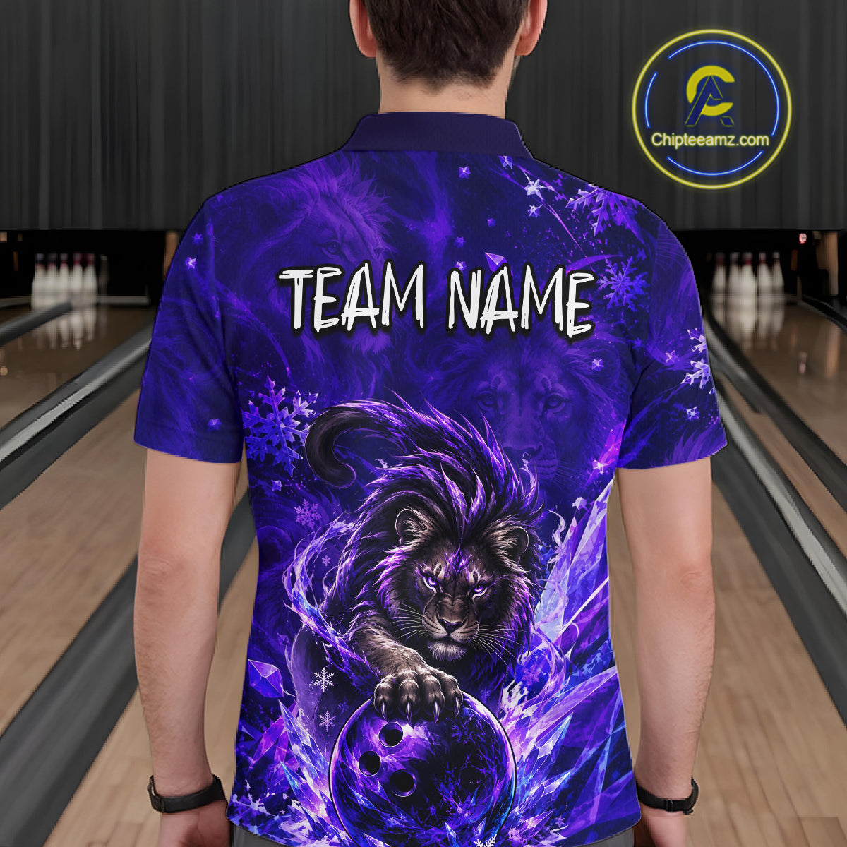 A man viewed from behind wearing a custom purple bowling-themed polo shirt with a graphic of a lion holding a bowling ball and the text 'TEAM NAME' printed on the back. The background shows a bowling alley with lanes and pins.