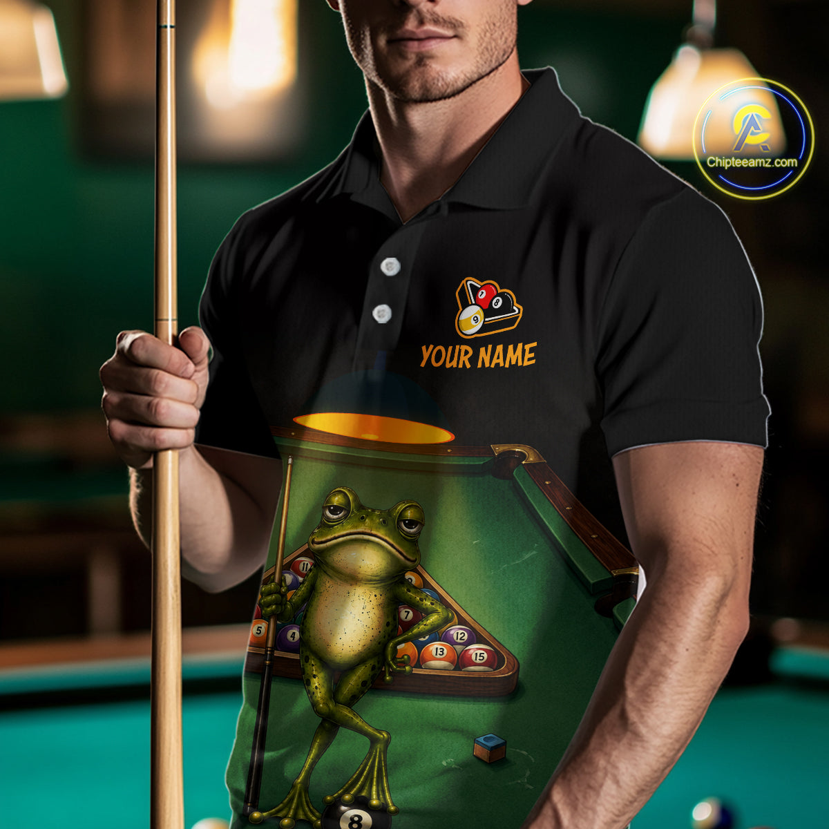 A man in a black polo shirt holding a pool cue, wearing a custom-printed belly patch or apron graphic featuring a green frog playing with billiards and the text 'YOUR NAME'.