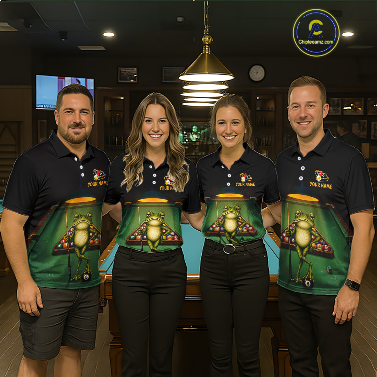 Four people standing indoors in front of a pool table, wearing matching dark polo shirts with a large green frog-and-betting-board graphic across the front. 
