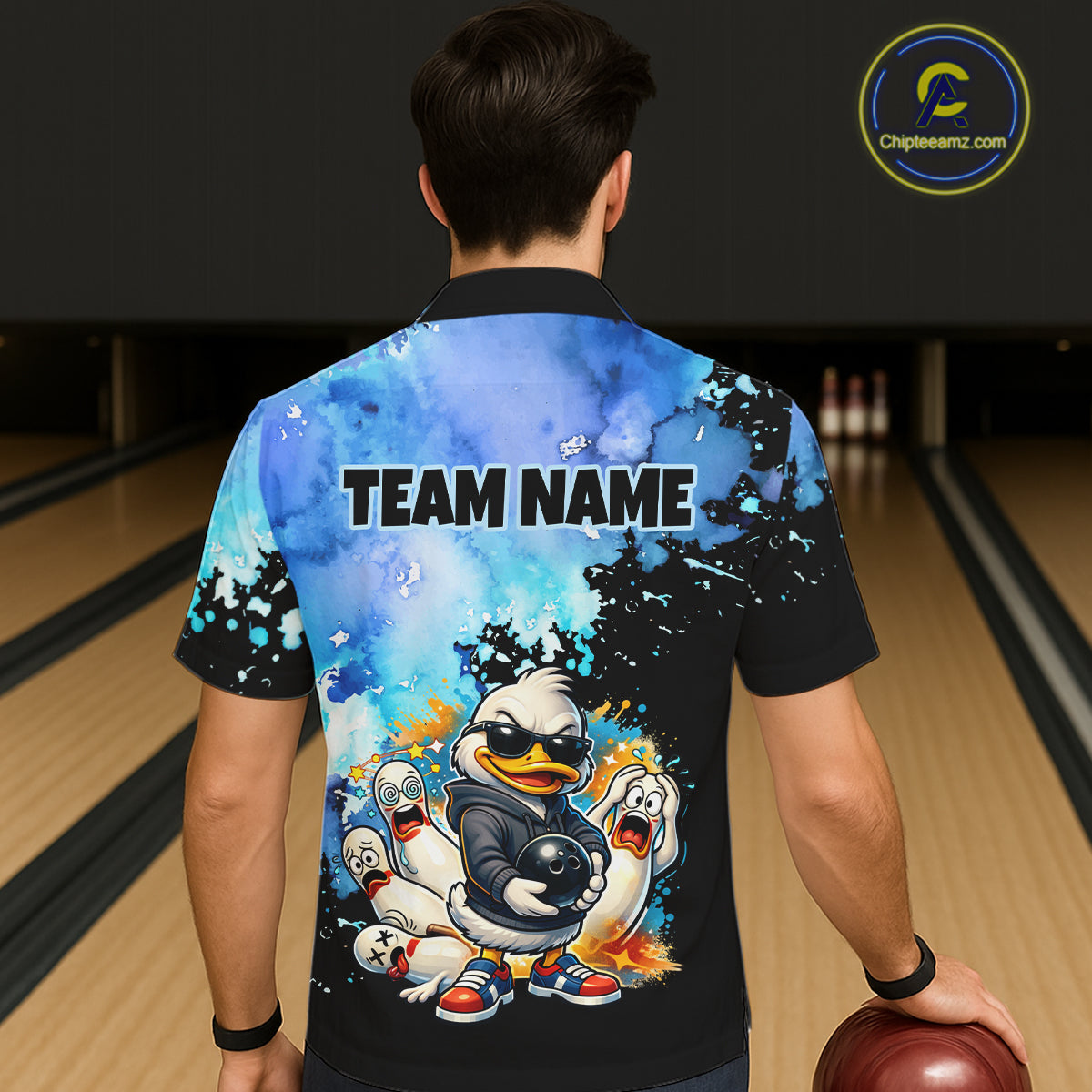 Person wearing a bowling shirt with cartoon duck design and 'TEAM NAME' text in a bowling alley.