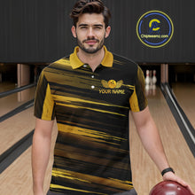Load image into Gallery viewer, Male model wearing a custom black gold bowling polo shirt front view featuring a gold bowling ball emblem, dynamic gold brush stroke pattern and striped design at the bowling alley