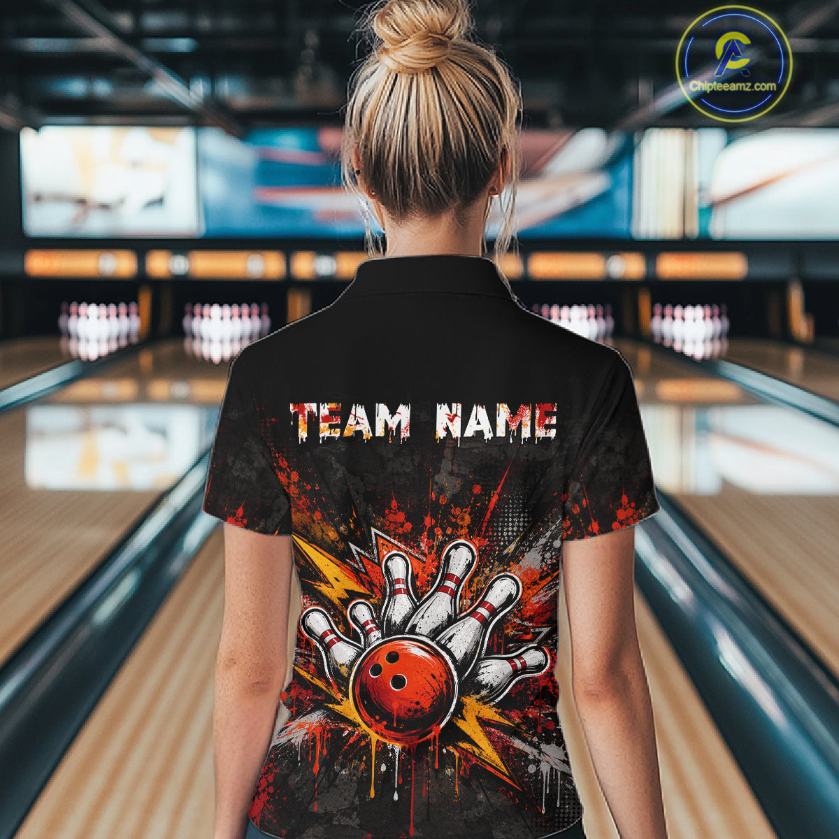 A woman viewed from behind wearing a black short-sleeve collared shirt with a bowling-themed graphic on the back. The design features the text 'TEAM NAME' above a hand striking a bowling ball with red, orange, yellow, and white paint-splatter effects.
