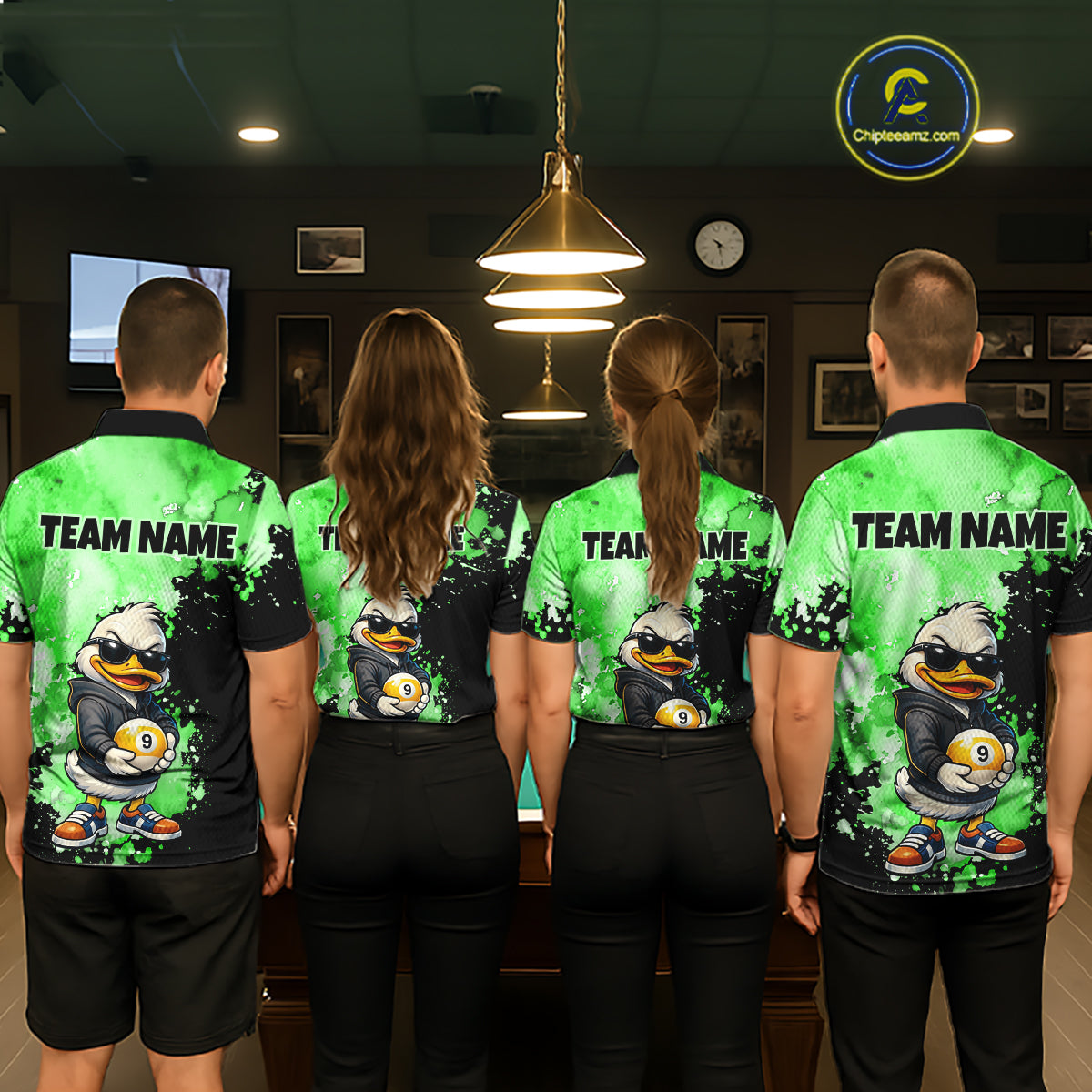Four people standing with their backs to the camera wearing matching custom short-sleeve athletic shirts in a dimly lit indoor venue. The shirts are bright green and black with a cartoon duck graphic and the text 'TEAM NAME' across the upper back.