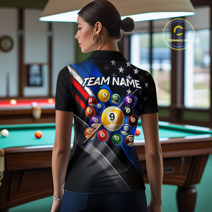 A woman viewed from the back wearing a black short-sleeve polo shirt with a colorful pool-themed graphic print featuring billiard balls, stars, stripes, and the text 'TEAM NAME'. The photo is taken in a billiards room with a pool table and lamp visible in the background.