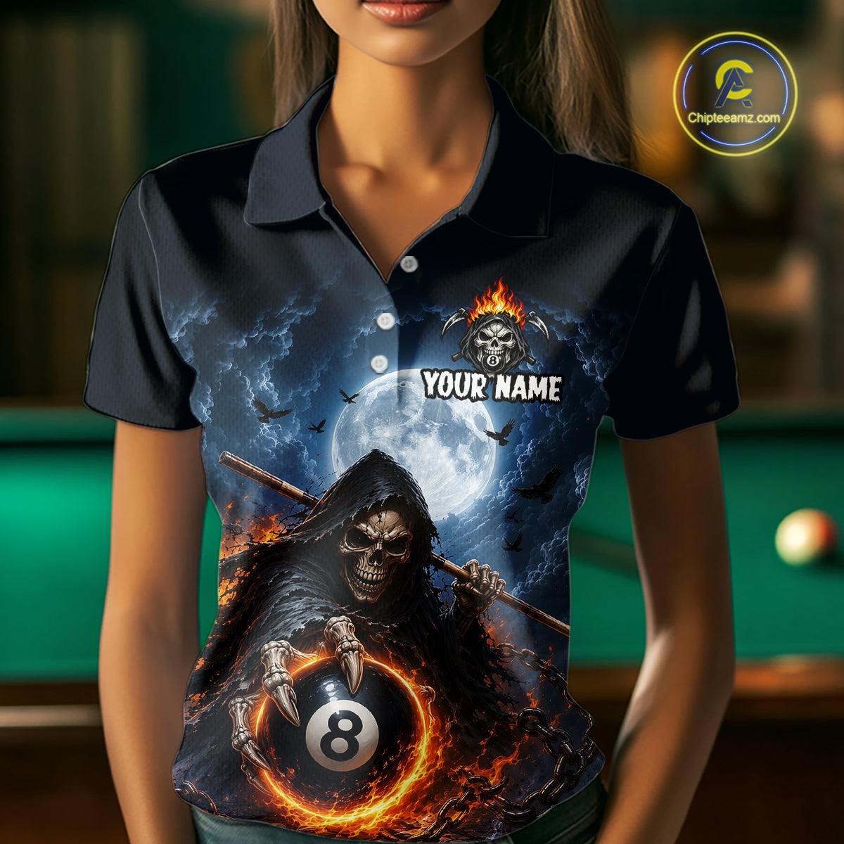 A woman wearing a dark navy polo shirt with a detailed graphic print of a grim reaper holding a flaming 8-ball in front of a full moon and bats. The shirt features a customizable placeholder text 'YOUR NAME' and a skull flame logo on the chest.