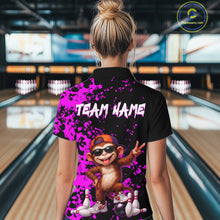 Load image into Gallery viewer, A woman viewed from behind wearing a black short-sleeve polo shirt with a bright purple splatter design, white 'TEAM NAME' text, and a cartoon monkey graphic in bowling lanes. The image is set in a bowling alley.