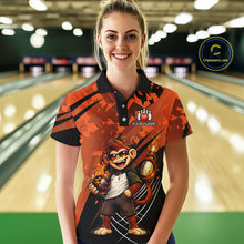 Load image into Gallery viewer, A woman wearing a custom orange and black bowling shirt with a cartoon monkey graphic, standing in a bowling alley. The shirt features a black collar, a custom logo with a paw print and the text 'YOUR NAME'