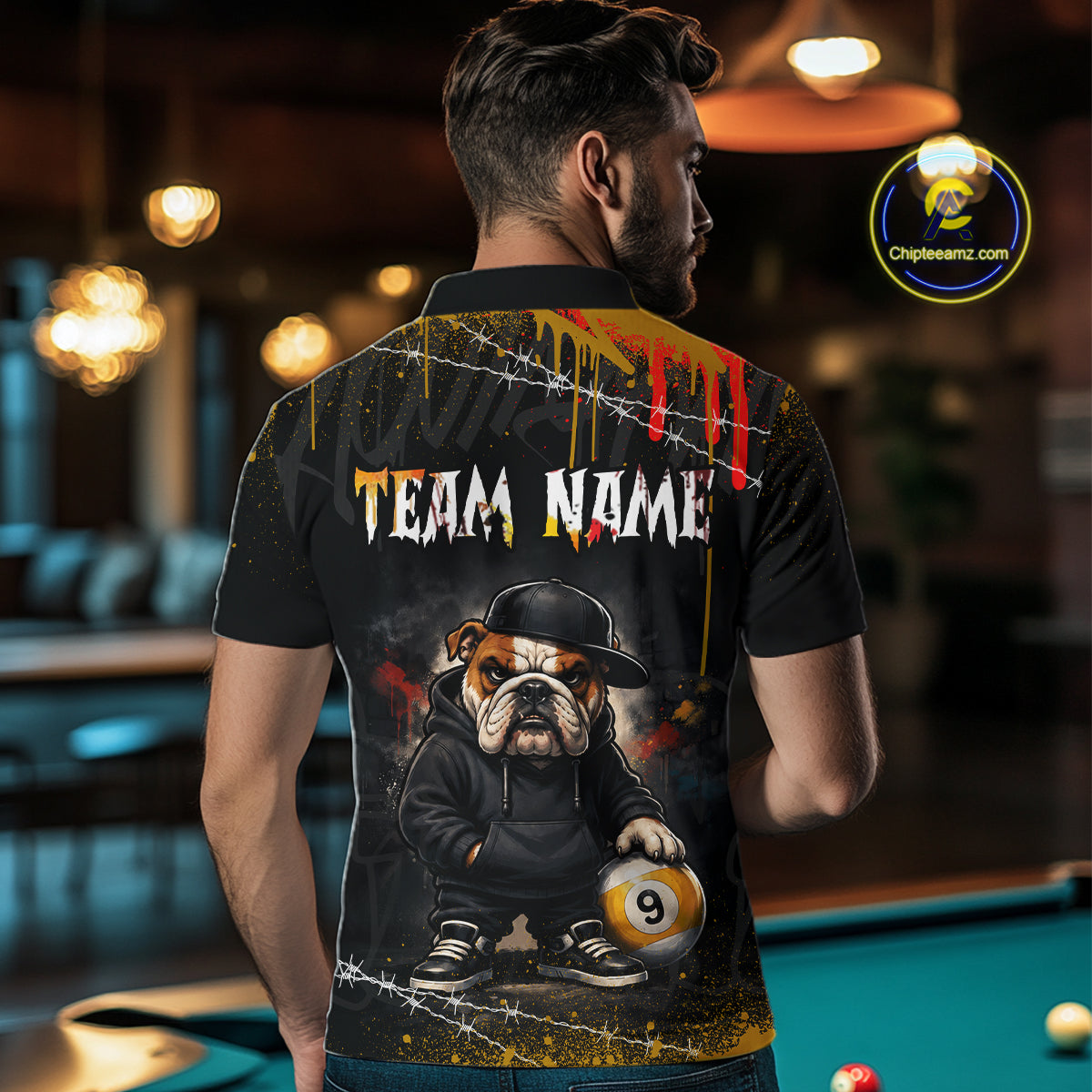 A man viewed from behind wearing a black short-sleeve polo shirt with a large custom graphic on the back. The graphic features the text 'TEAM NAME' in distressed white letters, a cartoon bulldog in a black hat and hoodie holding a pool ball, and yellow, red, and white paint drip details.