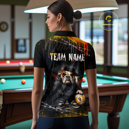 A woman stands in a billiards room wearing a black short-sleeve polo shirt with a custom graphic print. The back of the shirt features a cartoon bulldog in a black hat and jacket holding a 9-ball, with 'TEAM NAME' text and paint splatter details.