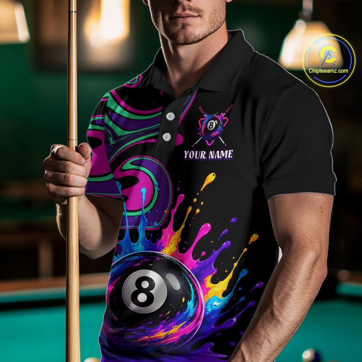 A man wearing a black polo shirt with a vibrant, colorful 3D-printed design featuring an 8-ball pool cue graphic, paint splatters, and a custom name placeholder on the chest. He is holding a pool cue in a dimly lit pool hall environment.