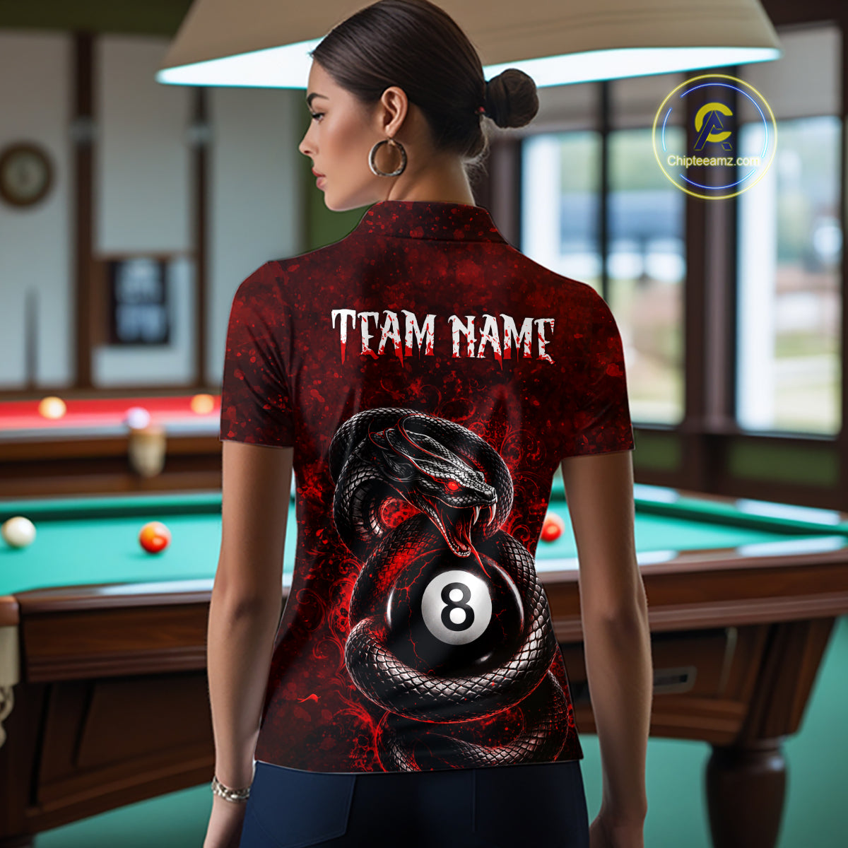 A woman stands with her back to the camera wearing a short-sleeve collared polo shirt with a red and black snakes wrapping around an 8-ball graphic, and the text 'TEAM NAME' printed across the upper back. The shirt is shown in a pool room setting with a green pool table and billiards visible in the background.