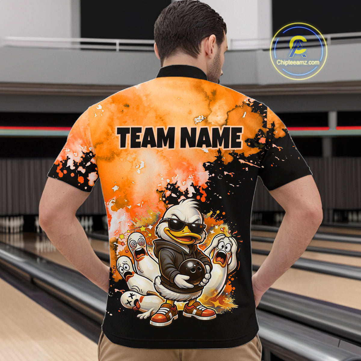 A man viewed from behind wearing a custom bowling shirt with a black and orange splattered background, cartoon duck graphics, and the text 'TEAM NAME' printed on the back. The shirt has short sleeves and a crew neck.