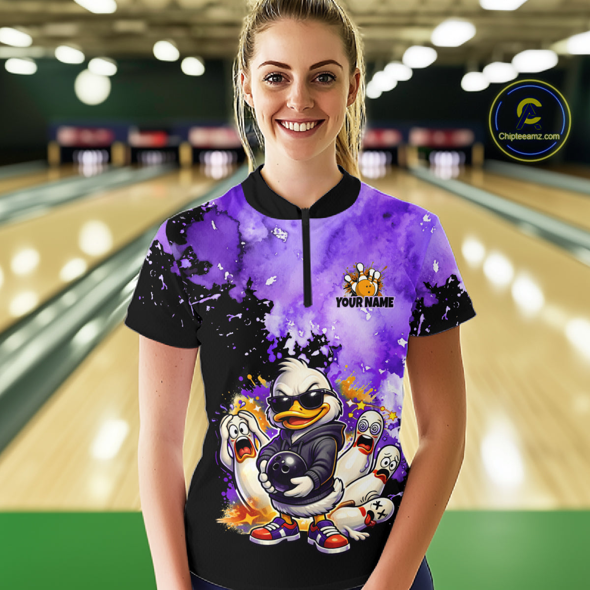 A woman stands in a bowling alley wearing a custom short-sleeve bowling shirt with a purple and black watercolor design, a cartoon duck mascot, and 'YOUR NAME' printed on the front. 