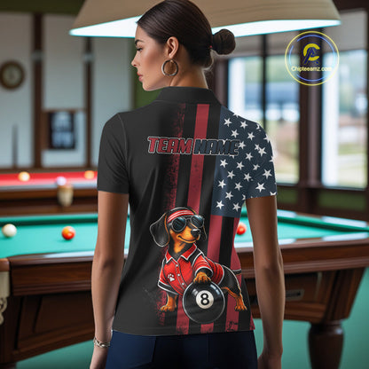 A woman stands in a billiards room wearing a black short-sleeve polo shirt with a custom American flag and dachshund graphic on the back. The shirt features a vertical split design with a red and black American flag on one side and a white star field on the other, with a dachshund wearing a red polo and sunglasses holding an 8-ball.