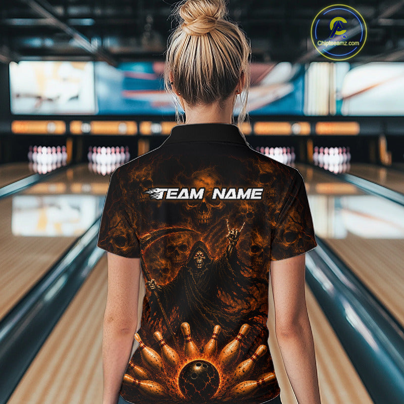 A woman viewed from behind wearing a black short-sleeve polo shirt with a fiery orange and brown grim reaper graphic and the text 'TEAM NAME' across the upper back, standing in a bowling alley.