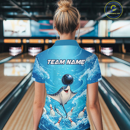 A woman viewed from behind wearing a blue bowling-themed short-sleeve collared shirt with a cartoon shark and bowling pins graphic on the back, standing in a bowling alley. The shirt has 'TEAM NAME' printed across the upper back.