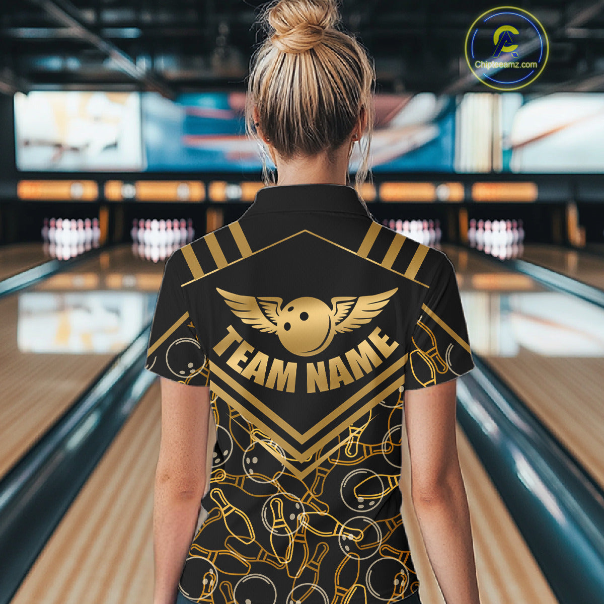Female model wearing a custom black gold bowling polo shirt back view displaying the personalized team name above a golden winged bowling ball graphic at the bowling alley