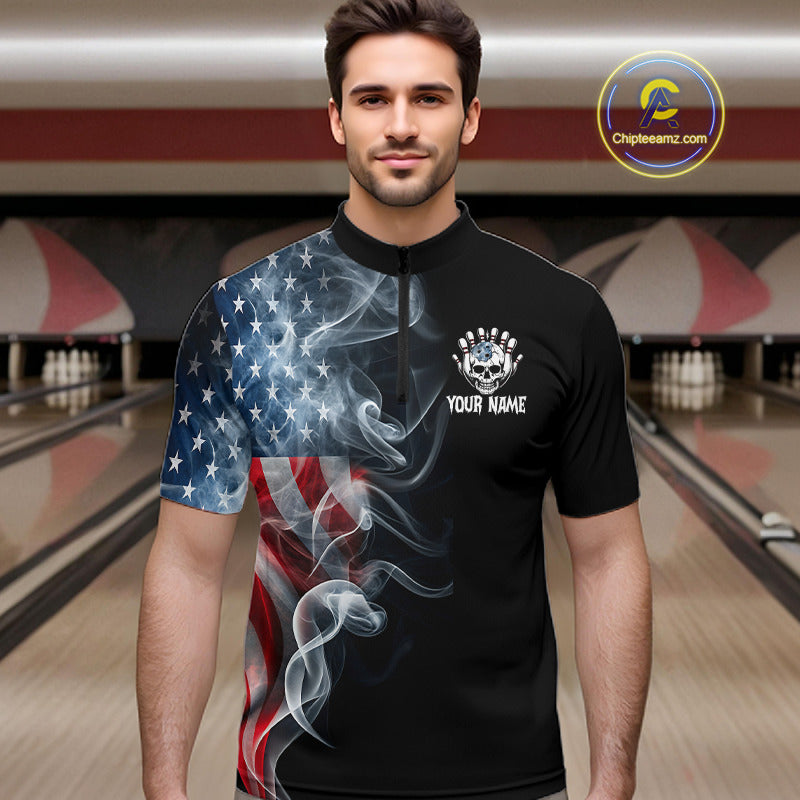 A man wearing a black short-sleeve bowling shirt with a split American flag and smoke graphic design, standing in a bowling alley. The shirt features a white skull and stars logo on the left chest with the text 'YOUR NAME'.