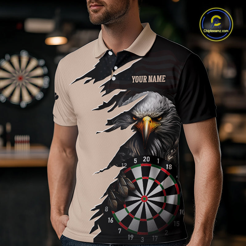 Person wearing a beige and black darts polo featuring a bald eagle, torn-flag graphics, dartboard designs, and custom team text.