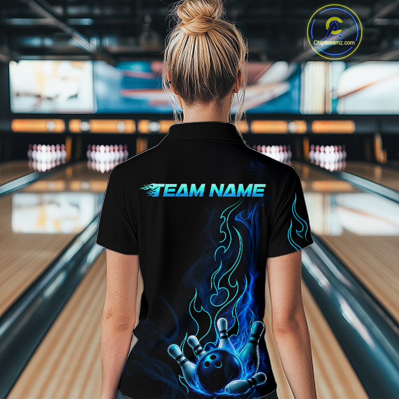 A woman viewed from behind wearing a black short-sleeve bowling polo shirt with a custom blue and teal flame graphic and 'TEAM NAME' text on the back, standing in a bowling alley.