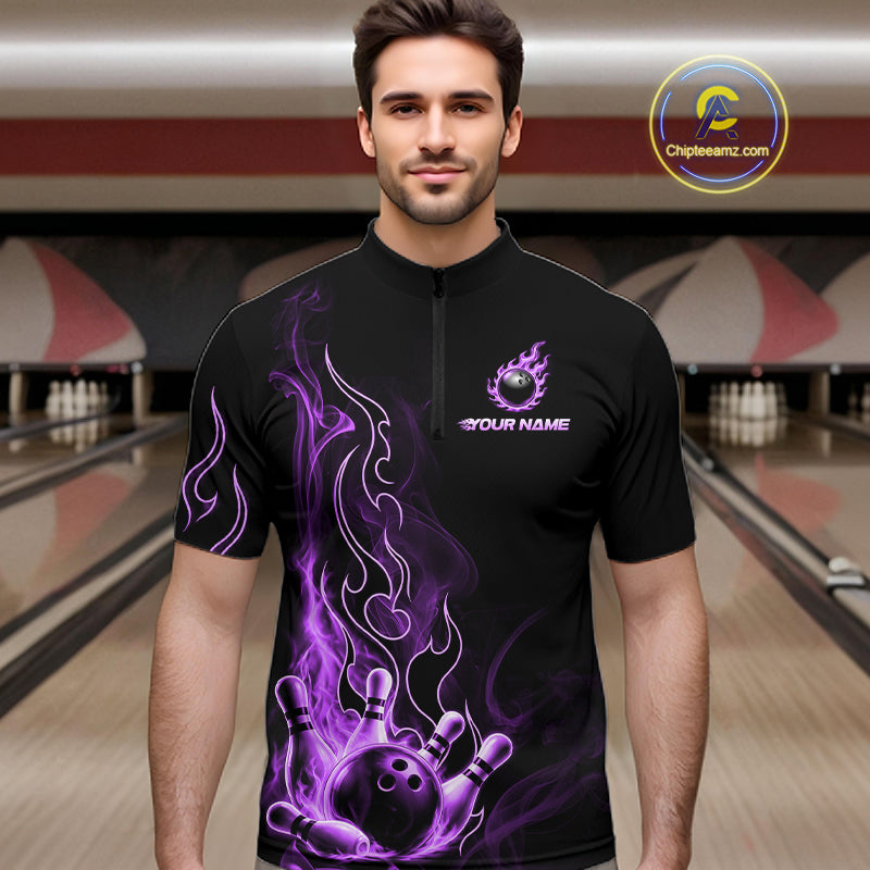 A man wearing a black short-sleeve bowling t-shirt with a purple flame and bowling ball graphic, standing in a bowling alley. The shirt features a mock logo on the left chest and 'YOUR NAME' on the right chest.