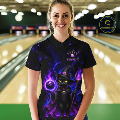 A woman stands in a bowling alley wearing a black short-sleeve polo shirt with a colorful graphic of a black cat dressed as a witch surrounded by purple magic, a bowling ball, and the text 'YOUR NAME'. 