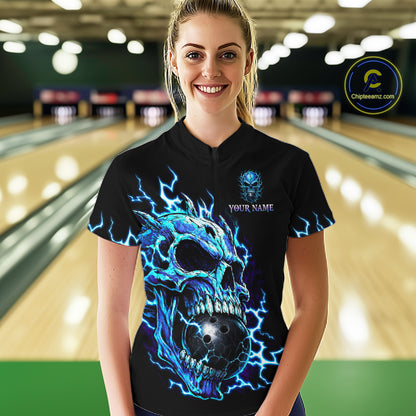 A woman stands in a bowling alley wearing a black short-sleeve polo shirt with a large blue and black skull graphic and lightning details, plus a small chest print reading 'YOUR NAME'. 